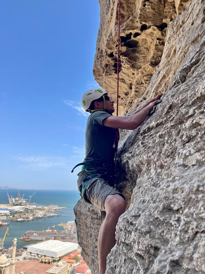A person rock climbing a cliff with a cityscape in the background. 4