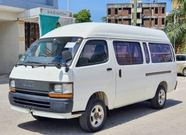 A white van parked on a paved surface with buildings in the background. 4