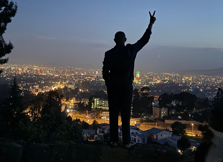 A silhouette of a person with a peace sign against a cityscape at dusk. 1