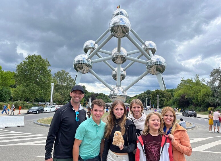 A group of people posing in front of a large metallic structure with spherical elements. 1