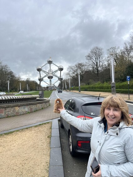 A person holding a dog near a car and a large metallic structure in the background. 3