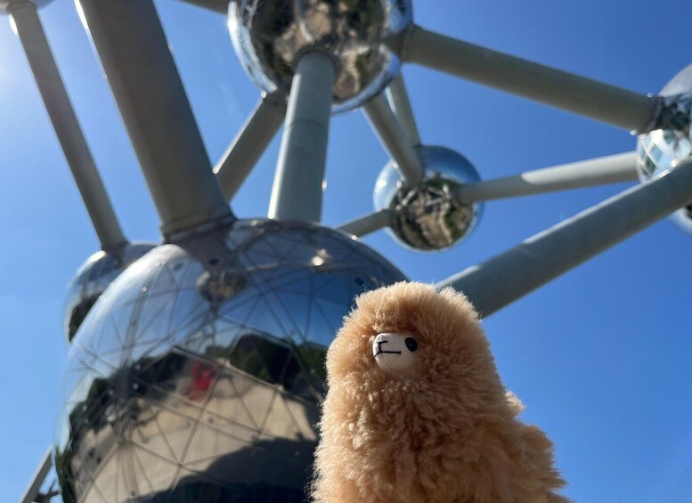 A fluffy brown toy with a white face and black eyes, positioned in front of a large, reflective spherical structure. 4