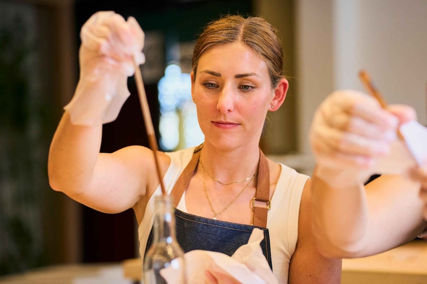 A person wearing a white shirt and denim apron, holding a bottle and a spoon, likely preparing food. 5