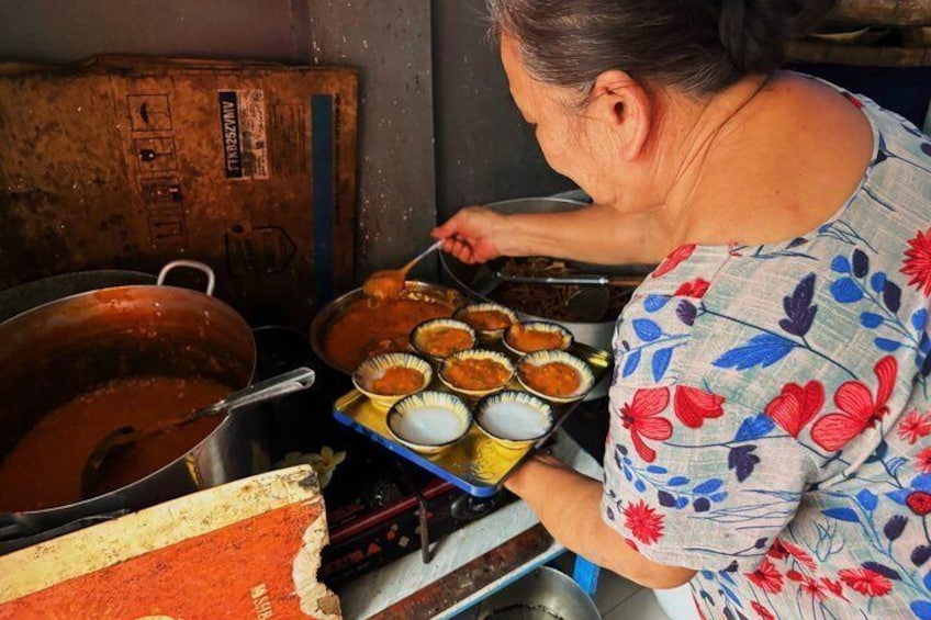 A person cooking in a kitchen with large pots and pans, a stove, and a tray of food. 1