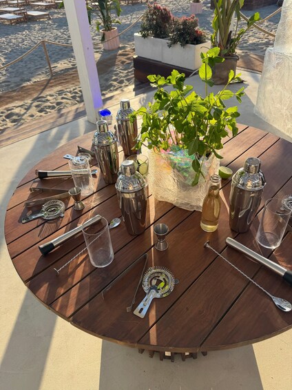 A round wooden table with cocktail-making tools, glasses, and a potted plant. 2