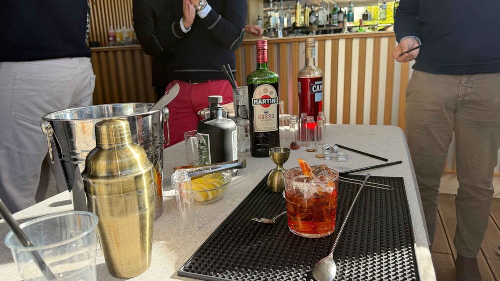 A bar setting with a martini bottle, a cocktail glass with a straw, and various bar tools on a table. 4