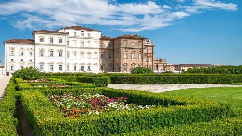 A large, historic building with manicured gardens and a clear blue sky. 1