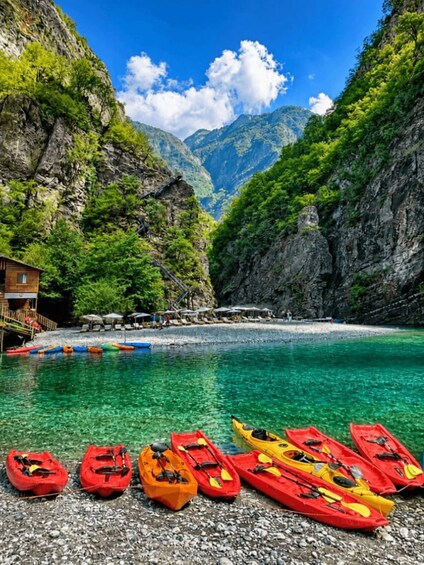 A clear turquoise sea, rocky cliffs, and a row of colorful kayaks lined up on a pebble beach. 4