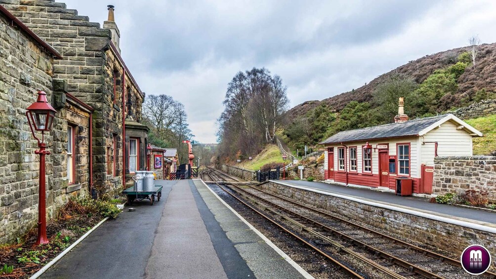 A railway station with stone buildings, a platform, and multiple tracks. 3