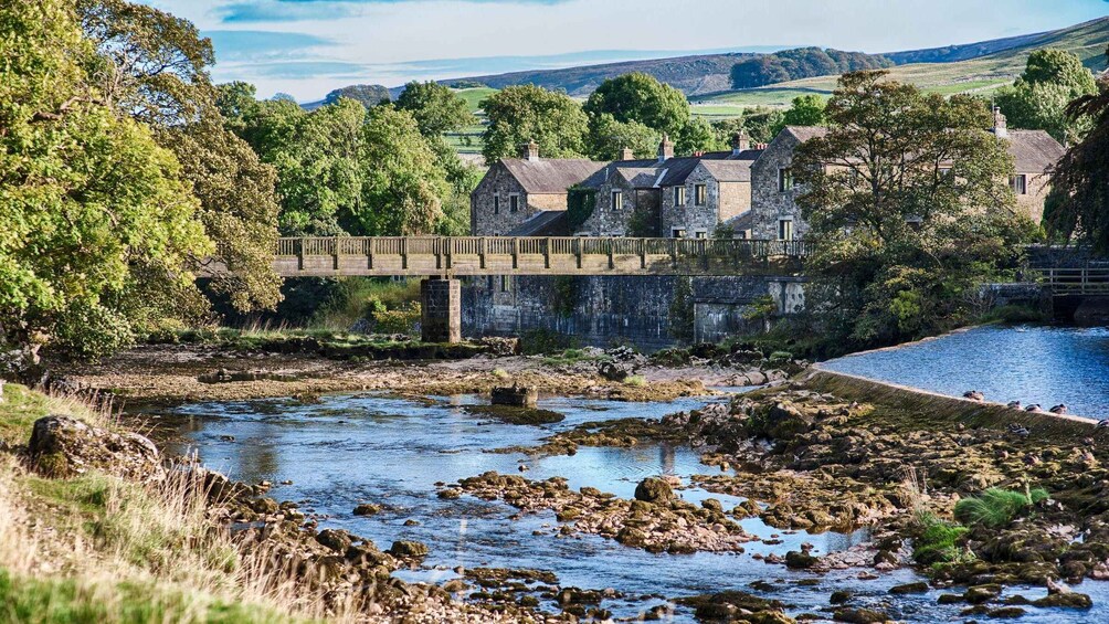 A stone bridge over a rocky river, surrounded by lush greenery and stone buildings. 2