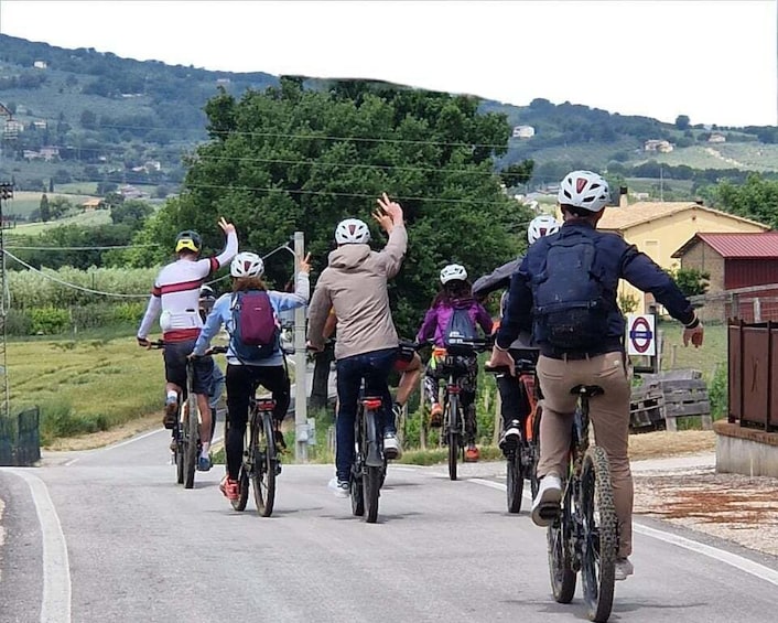 A group of cyclists on a paved road with a rural landscape in the background. 1