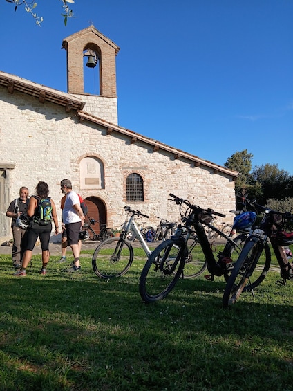 A stone building with a bell tower, bicycles, and people walking. 5