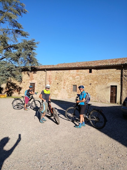Three cyclists standing next to their bikes in front of a stone building with a tiled roof. 4