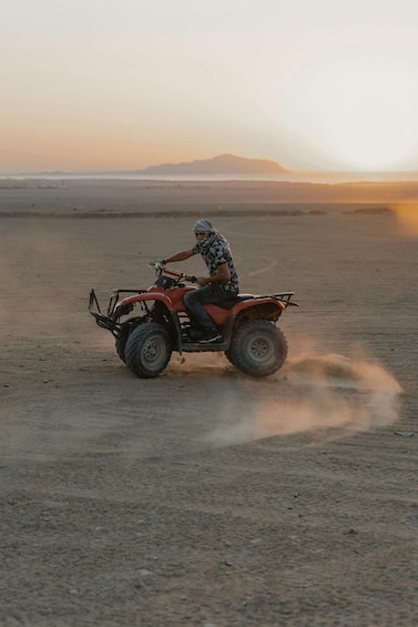 A person riding an ATV on a sandy beach with a mountain in the background. 4