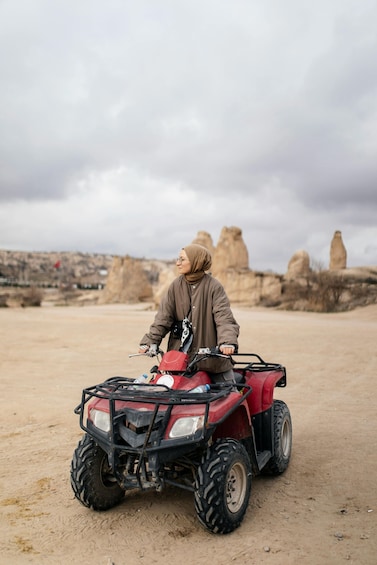 A person on a red ATV in a desert with rock formations in the background. 3