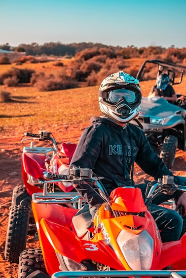 A person on a red ATV in a desert landscape. 1