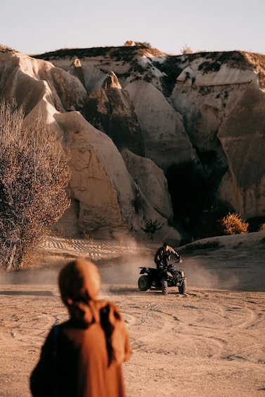 A person riding an ATV on a dirt path with rocky terrain and sparse vegetation. 2