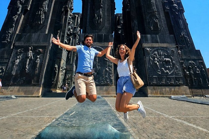 A couple jumping in front of a large, detailed monument with bas-relief sculptures. 4
