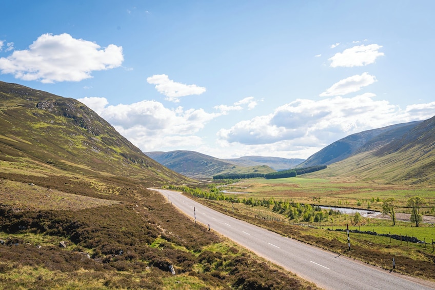 A winding road through a hilly landscape with a clear sky and scattered clouds. 1