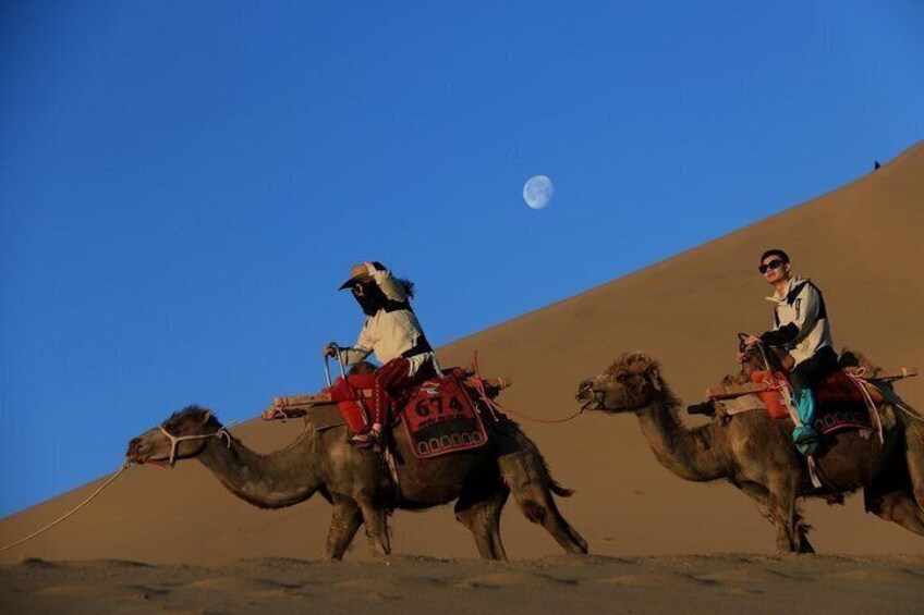 Deux chameaux, chacun monté par un cavalier, gravissent une dune de sable sous un ciel dégagé. 5
