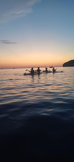 A sunset over a calm sea with several kayaks and a distant ship. 4