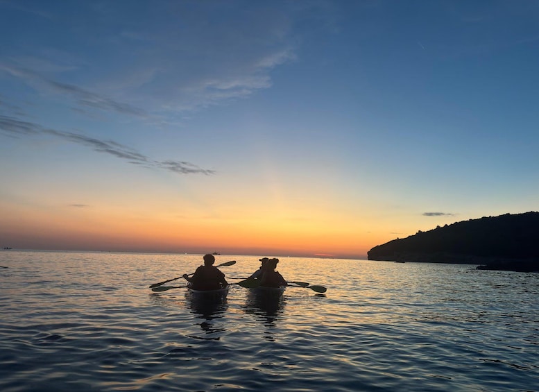 Two people kayaking on calm water during sunset. 2