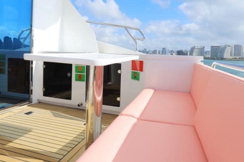 Cubierta de barco con toldo blanco, zona de estar acolchada y vista de un horizonte urbano al fondo. 2