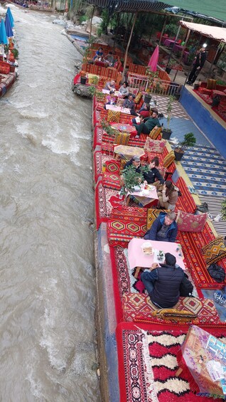A river with boats decorated with colorful fabrics and people dining on the riverbank. 5