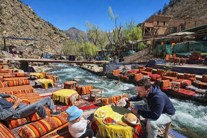 A riverside seating area with colorful cushions and tables, a bridge, and a mountainous backdrop. 4