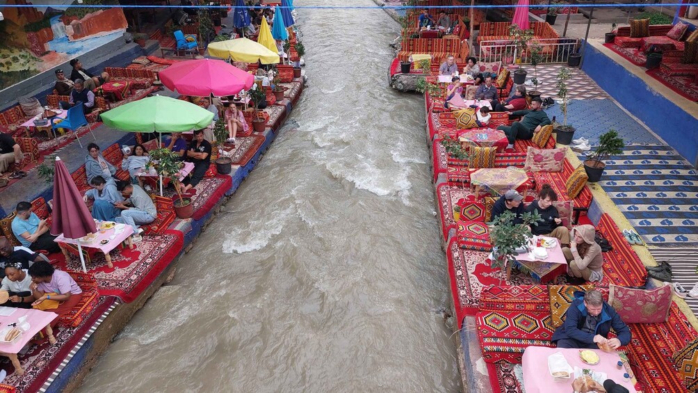 A river with boats and people dining on the banks. 3