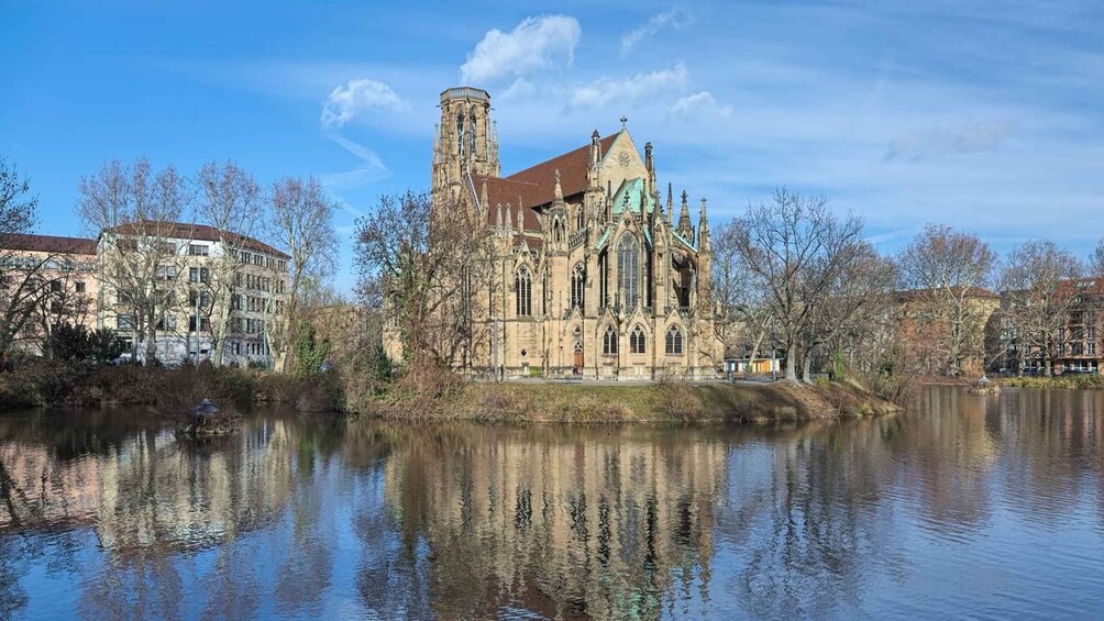 A historic church with a tall tower and Gothic architecture, surrounded by a calm river and leafless trees. 3