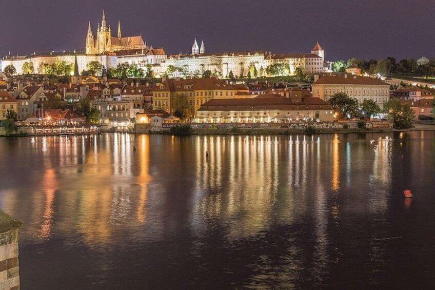 Vue nocturne d’une ville historique, avec un château et une cathédrale imposants qui se reflètent sur les eaux calmes d’une rivière. 2