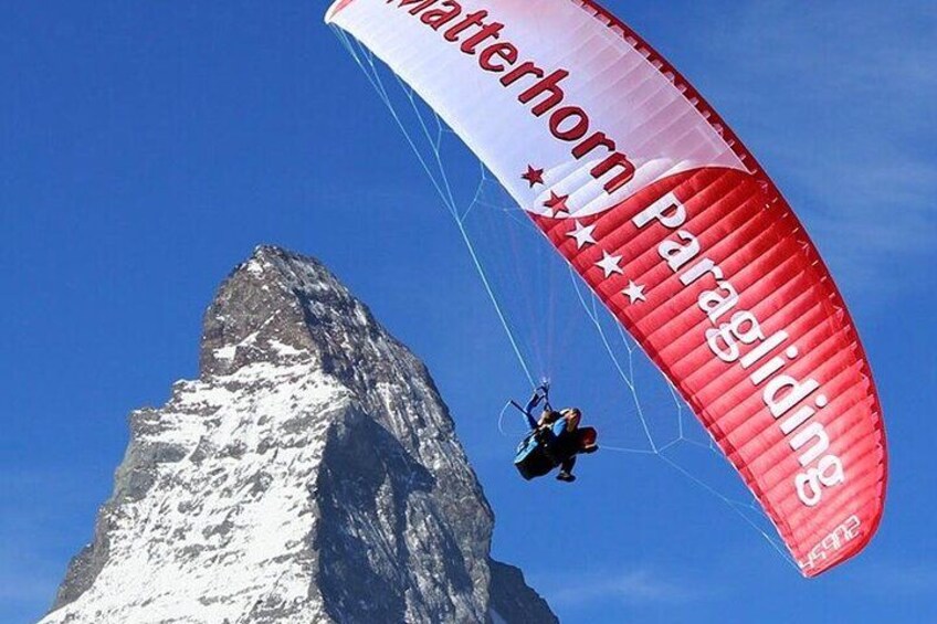 Un parapentista con un paracaídas rojo y blanco vuela cerca de una montaña nevada. 1