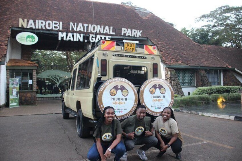 Un véhicule de safari arborant le logo « PAWONIA SAFARIS » est garé devant la porte principale du parc national de Nairobi. 1