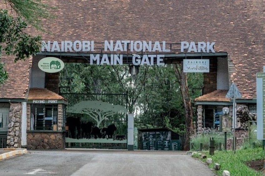 The Nairobi National Park main gate with a stone facade, a green gate, and a sign indicating a paying point. 2