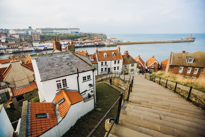 A coastal town with terracotta-roofed buildings, a stone staircase, and a pier extending into the sea. 3