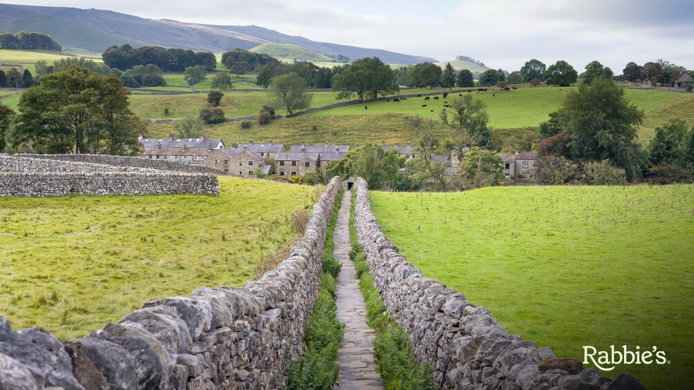 A stone wall leading to a village with houses and green fields. 1