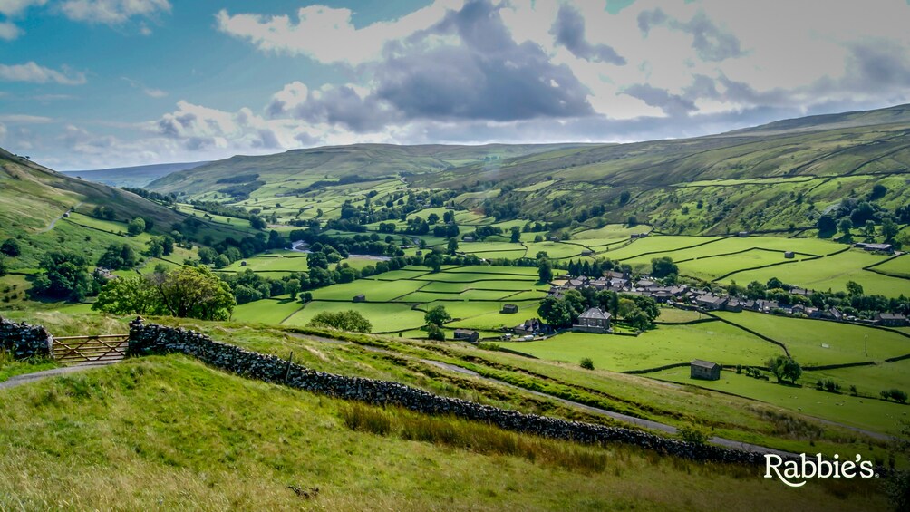 A rural landscape with rolling hills, a stone wall, and a small village. 5