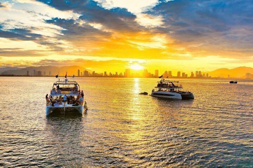 A sunset over a body of water with two boats and a city skyline in the background. 1