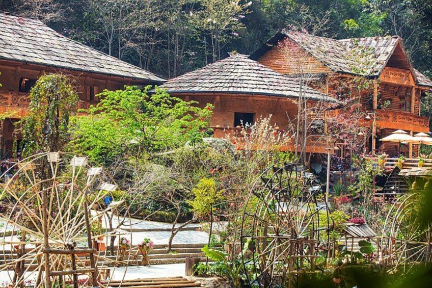 Traditional wooden houses with thatched roofs, surrounded by lush greenery and a small water wheel. 2