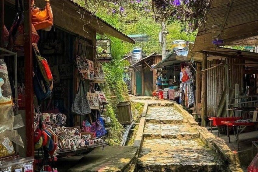 A narrow alleyway with shops on either side, wooden structures, and a stone pathway. 1