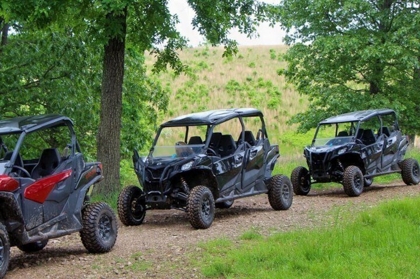 Three off-road vehicles parked on a dirt path in a grassy area with trees. 3