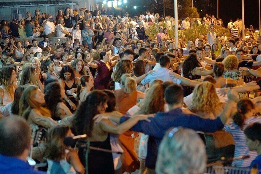 A large crowd of people gathered outdoors, some standing and some sitting, with a stage in the background. 4