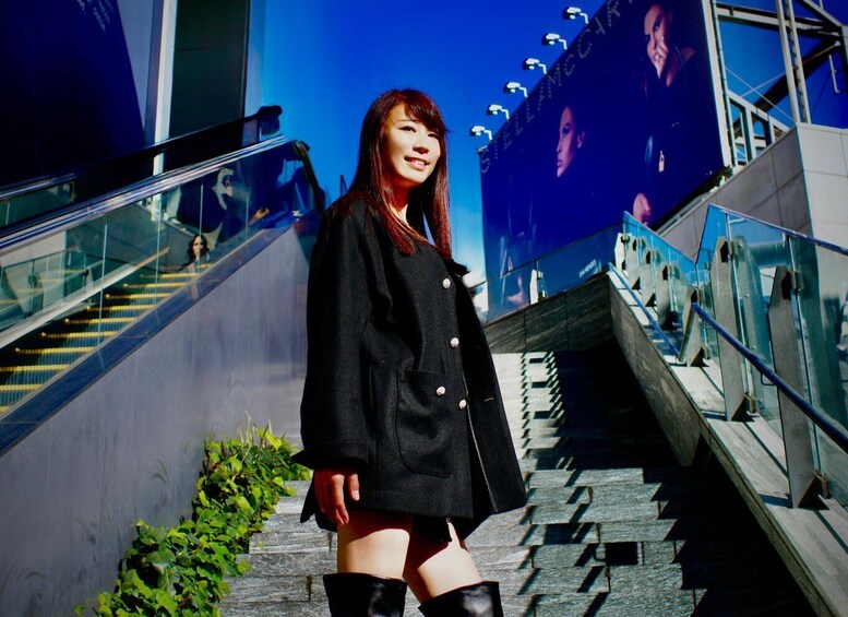 A person walking down a staircase in a modern building with glass railings and a large digital billboard in the background. 3