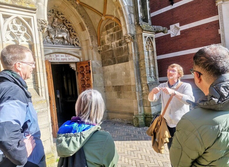 A group of people standing in front of a historic building with ornate stonework and a wooden door. 4