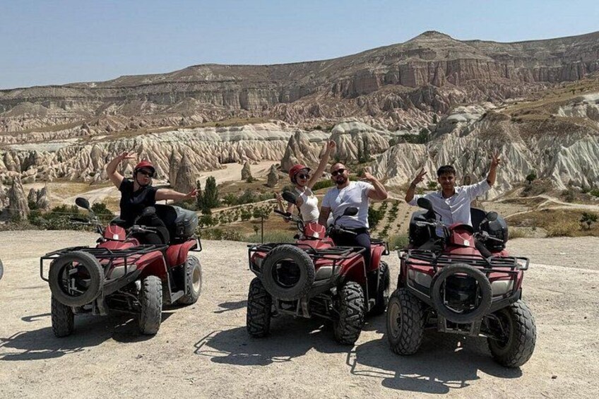Three people on red quad bikes in a desert landscape with rocky formations. 1