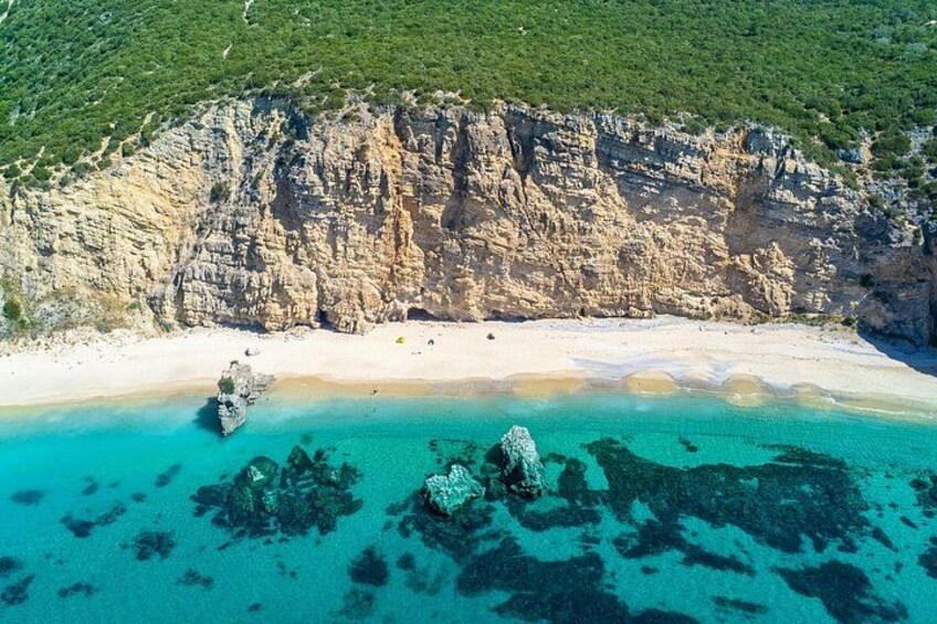 Un paysage côtier caractérisé par une plage de sable, des eaux turquoise et limpides, et des affleurements rocheux. 1