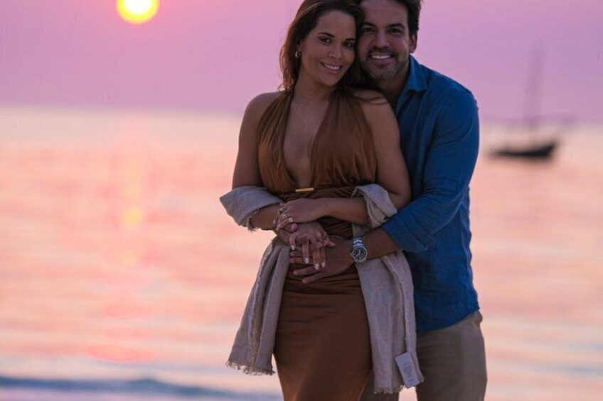 Una pareja abrazándose al atardecer, con un barco al fondo. 1
