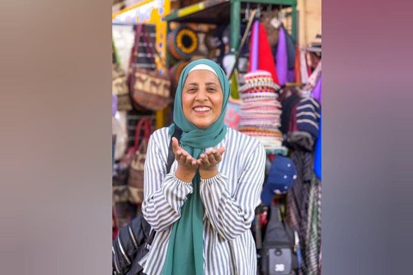 A person in a market with colorful bags and textiles in the background. 1