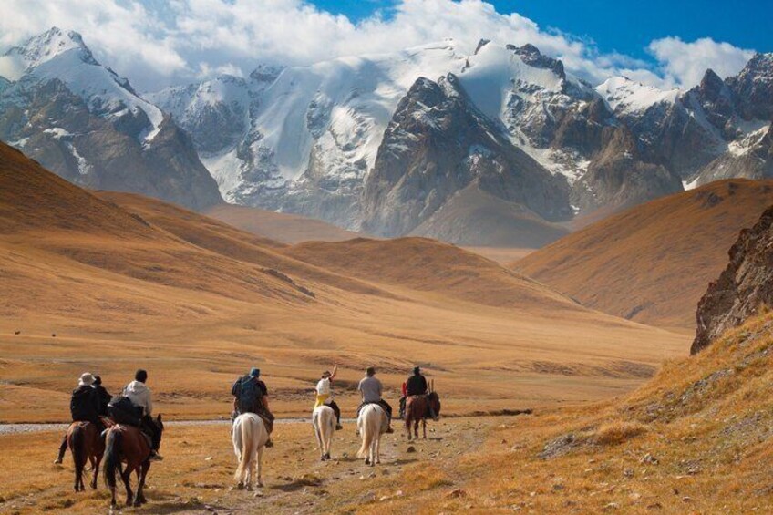 Un grupo de personas a caballo en un paisaje montañoso con picos nevados al fondo. 1
